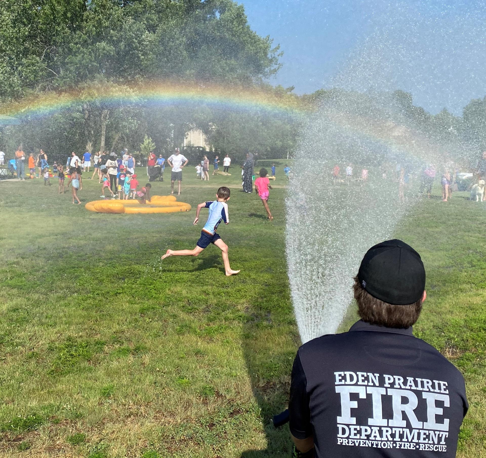 A rainbow forms as a Firefighter is spraying a hose during pop-up splash pad.