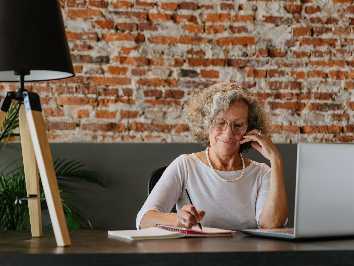 Women on Cell Phone WIth Laptop and Writing in Notepad